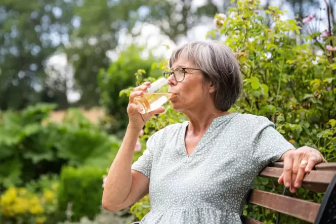Eine Frau sitzt im Freien und trinkt aus einem Glas
