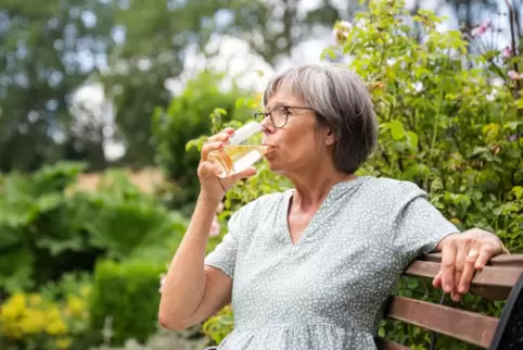 Eine Frau sitzt im Freien und trinkt aus einem Glas