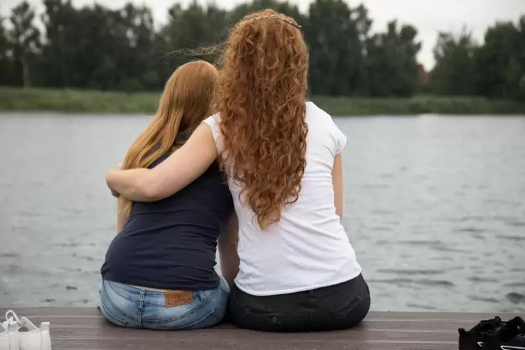 Zwei junge Frauen sitzen auf einem Steg einem See