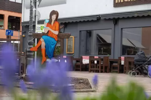 Die Kaffee trinkende Frau fällt direkt wegen ihrer farbenfrohen Kleidung auf. Sie sitzt in der St.-Michael-Straße vor dem Restau