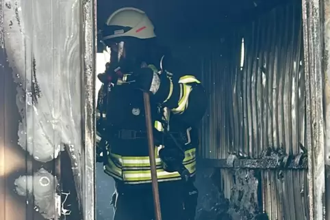 Eine Einsatzkraft der Feuerwehr steht im Innern des ausgebrannten Bauwagens.
