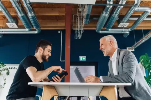 Jüngerer und älterer Mensch sprechen in modernem Büro miteinander