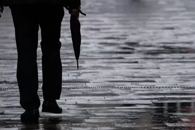 Ein Passant geht mit Regenschirm in der Hand durch Mainz