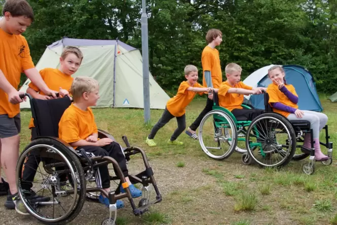 Die Probleme behinderter Menschen kennenlernen: Teilnehmer des Jugendzeltlagers üben den Umgang mit Rollstühlen auf dem Weg zum