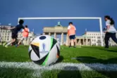 Kinder spielen in Berlin auf dem Kunstrasen vor dem Brandenburger Tor mit dem riesigen Fußballtor hinter dem offiziellen Ball fü