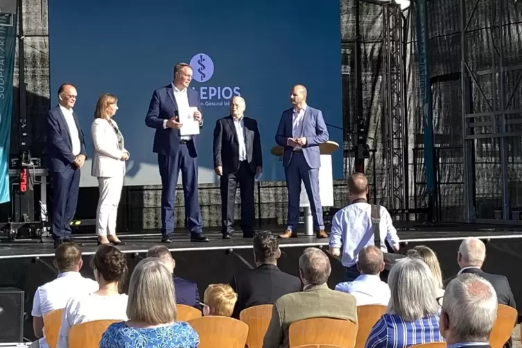 Ministerpr&auml;sident Alexander Schweitzer (Mitte) &uuml;bergibt den F&ouml;rderbescheid &uuml;ber knapp 65 Millionen Euro. Mit ihm auf der B&uuml;hne s