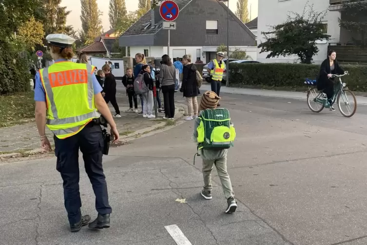 Viel los auf der Kreuzung: Polizistin hilft einem Kind &uuml;ber die Stra&szlig;e. 