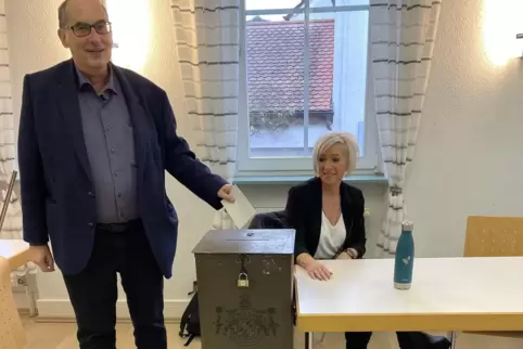 Windens Ortsbürgermeister wirft seinen Stimmzettel in die nostalgische Wahlurne, über die seine Beigeordnete Nadja Renz kritisch
