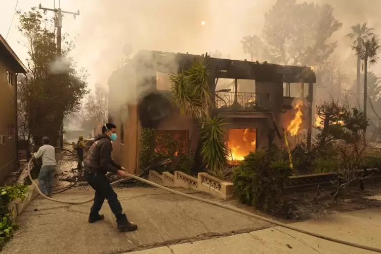Fu&szlig;g&auml;nger helfen einem Feuerwehrmann, einen Schlauch zu auszulegen, w&auml;hrend ein Wohnhaus in Altadena brennt. 
