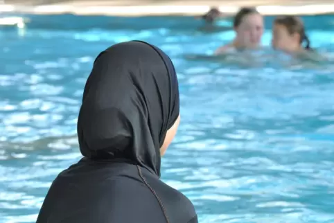 Eine muslimische Schülerin sitzt am Rande eines Schwimmbeckens. Vergleichsweise eng anliegende Burkinis sind auch kein Problem.