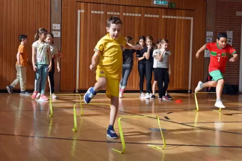Die Kinder überspringen kleine Hürden in der Sporthalle. 