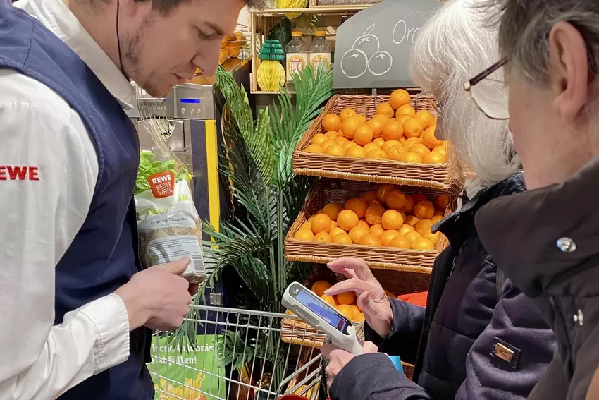 Rewe-Mitarbeiter Christian Kuhn hilft den Seniorinnen bei ihrer Handscanner-Premiere. Auf diesen sieht man auch gleich den aktue