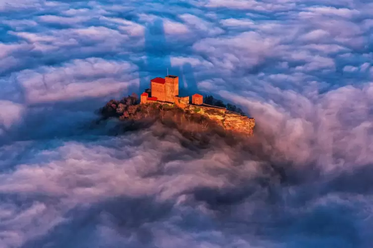 Die Kaiserburg, der Trifels, ragt aus dem Nebelmeer und zeigt ihre Dominanz mit einem gro&szlig;en Schattenwurf. 