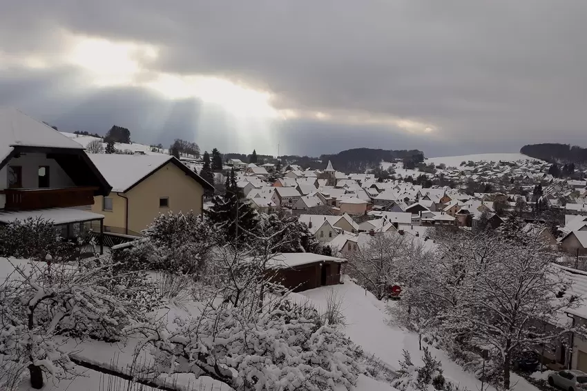Die Sonne bricht auf dem Bild von Josefa Thul durch die Wolken, darunter liegt das verschneite Breitenbach.