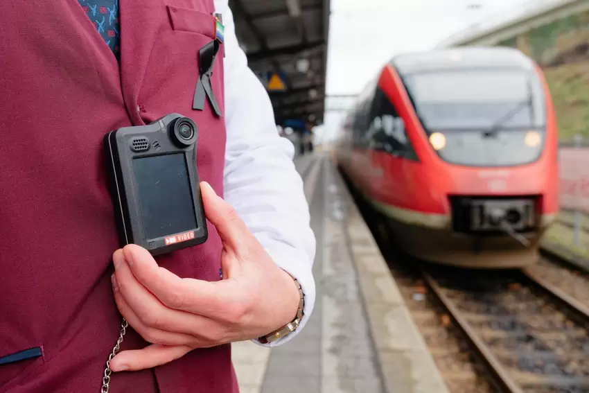 Ein Kundenbetreuer steht bei einem Pressetermin der Deutsche Bahn (DB) auf einem Bahnsteig neben einem Regionalzug und trägt ein