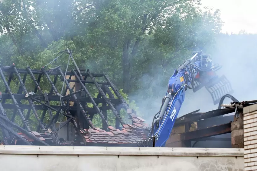 Links der verkohlte Dachstuhl des Wohnhaus-Längsbaus. Rechts macht sich der Bagger an der Lagerhalle zu schaffen.