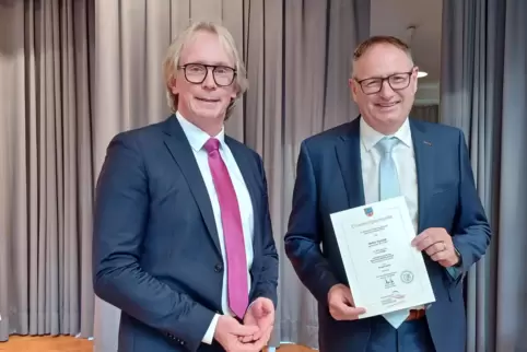 Walter Schmitt (rechts) zeigt seine Ernennungsurkunde zum Bürgermeister der Verbandsgemeinde Dannstadt-Schauernheim. Links sein 