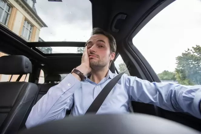 Ein Mann am Steuer fasst sich ins Gesicht