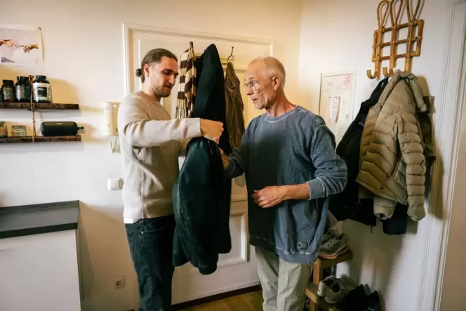 Ein junger Mann hilft einem Senior die Jacke anzuziehen