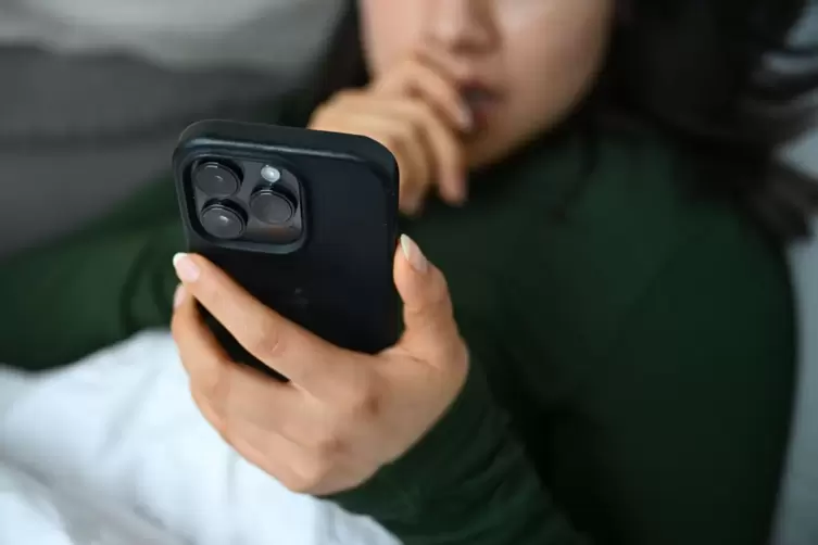 Eine junge Frau liegt mit ihrem Handy auf der Couch