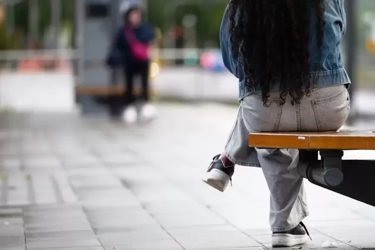 Eine junge Frau sitzt an einer Haltestelle auf einer Bank