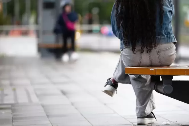 Eine junge Frau sitzt an einer Haltestelle auf einer Bank