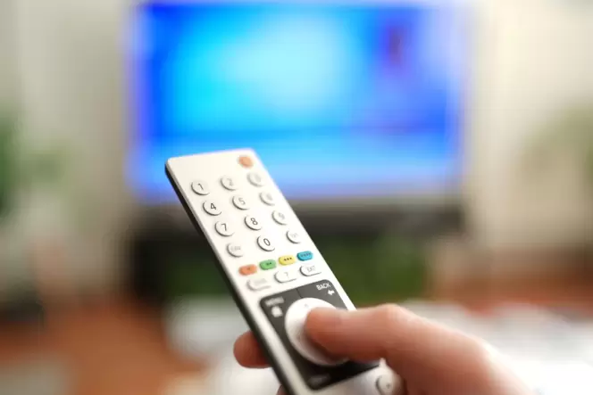 Ein Mann drückt einen Knopf auf einer TV-Fernbedienung