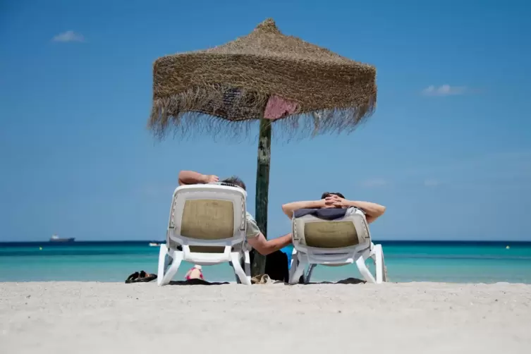 Touristen liegen am Strand unter einem Sonnenschirm