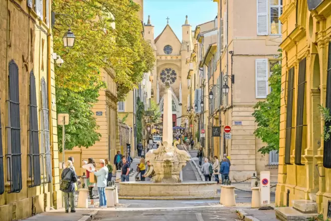 Der Delfinbrunnen in der Altstadt von Aix-en-Provence. Im Hintergrund die Kirche des heiligen Johannes von Malta.