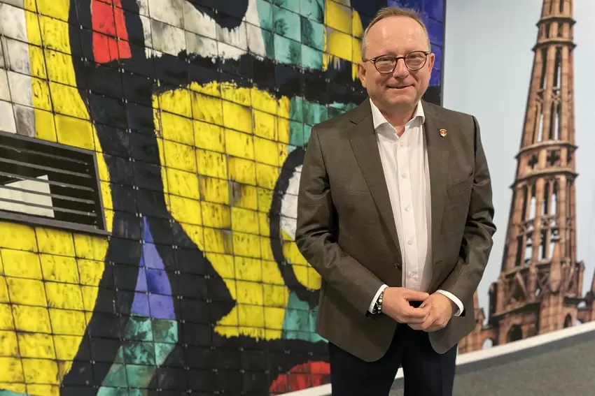 Klaus Blettner vor einer neuen Bildercollage im Foyer, das zu seinem Büro führt.