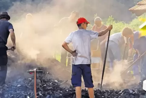 Beim Öffnen des Meilers stehen die Helfer in einer Qualm- und Rußwolke.