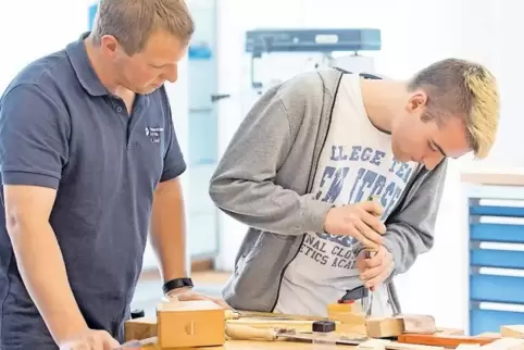 Ausbilder Kevin Groß (links) guckt zu, wie Marcel Zabel an einem Holzstück arbeitet.