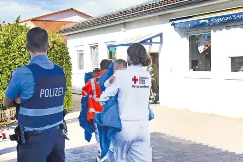 Die Einsatzkräfte bringen die Kinder in Decken eingewickelt in einer benachbarten Halle in Sicherheit, wo sie vor dem Wind gesch