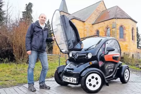 Steffen Glombitza mit einem Elektroauto vor der Kirche.