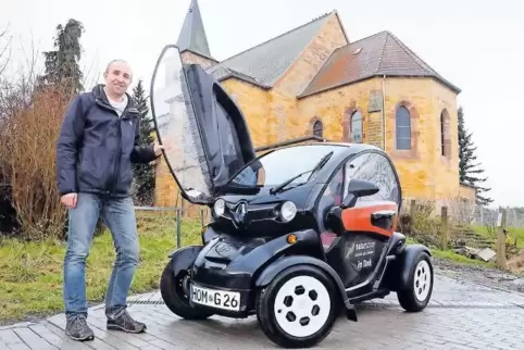 Steffen Glombitza mit einem Elektroauto vor der Kirche. Er glaubt, dass Menschen auch über Umweltprojekte und Konsumkritik einen