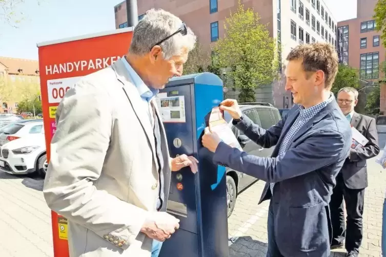 Bestücken den ersten Parkscheinautomaten mit Hinweiszetteln zum Handyparken: Baudezernent Peter Kiefer (links) und Philipp Zimme