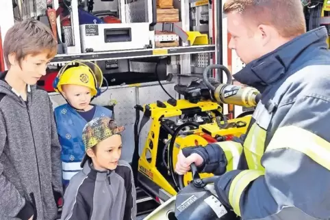 Feuerwehrmann Yannik Munzinger (rechts) zeigt jungen Besuchern einen Rettungsspreizer vor einem Einsatzfahrzeug.