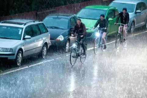 Radfahrer fahren bei kurzem Starkregen und Gewitter an parkenden Autos vorbei.  Foto: dpa