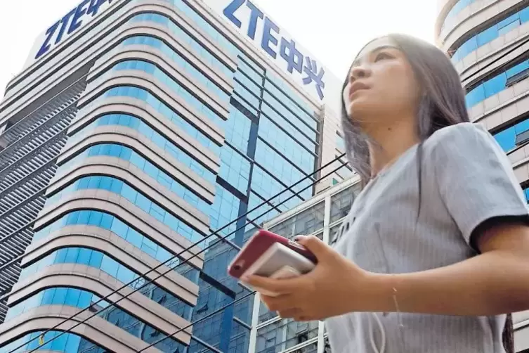 Peking: Eine Frau mit einem Smartphone in der Hand geht an einem Gebäude des chinesischen Netzwerk-Ausrüsters und Smartphone-Anb