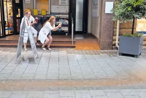 Anja König und Anna Ziereisen halten die Überschwemmungen in der Grünstadter Fußgängerzone mit der Kamera im Mobiltelefon fest.