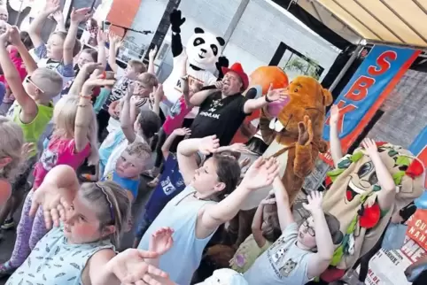 Nils Nager, Markus Becker, der Panda und verschiedene Früchtchen feiern mit den Kindern beim SBK für einen guten Zweck.