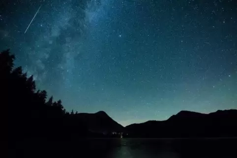 Eine Sternschnuppe leuchtet neben der Milchstraße am Himmel über dem Walchensee. Foto: dpa