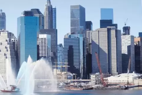 Ein Feuerwehrboot verspritzt Wasser in bunten Farben auf dem East River vor der Skyline von Lower Manhattan, wo sich die Wall St