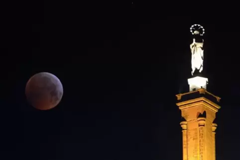 Der rötlich schimmernde Vollmond, ein sogenannter «Blutmond», steht hinter der Mariensäule in Trier.  Foto: Harald Tittel/dpa 