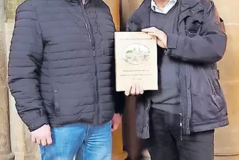 Genealoge Markus Zimmer (links) überreicht dem evangelischen Pfarrer Johannes Hülser das Familienbuch.
