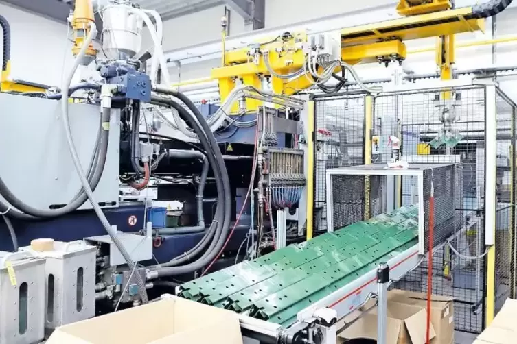 Die Spritzgussmaschine, auf der Teile f&uuml;r die Werkbank gefertigt werden. Das farblose PP-Granulat wird &uuml;ber Rohrleitungen zugef&uuml;
