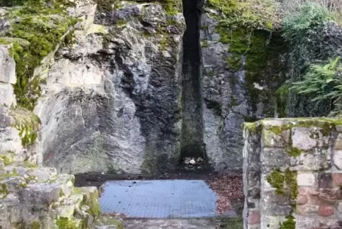 Das Foto zeigt die mit einem Stahlgitterrost abgedeckte Zisterne der Ruine Falkenstein, im Hintergrund (etwas rechts der Mitte) 
