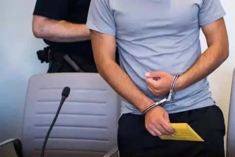 Der Angeklagte steht mit Handschellen im Gerichtssaal. 