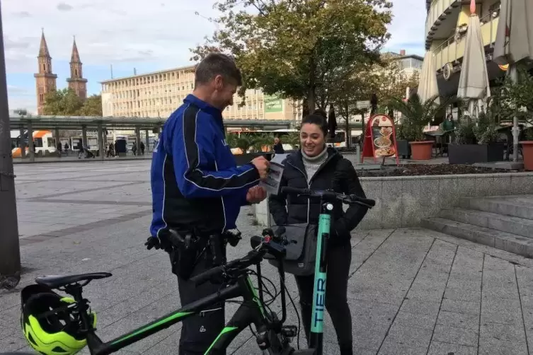 Polizeikommissar Christian Hein gibt einer E-Roller-Fahrerin einen Fyler mit, der zusammenfasst, was erlaubt und was verboten is