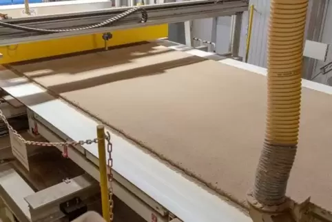 Drei mit Klebstoff vermischte Schichten mit unterschiedlich großen Spänen – der Kuchen – werden auf ein Transportband gestreut.